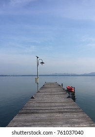 Old Small Wooden Dock Stretching In To The Sea With Blue Sky And Silhouette Of Mountain In Background. No People.