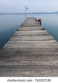 Old Small Wooden Dock Stretching In To The Sea With Blue Sky And Silhouette Of Mountain In Background. No People.