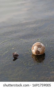 Old Soccer Ball Floating Discarded In Shallow Water