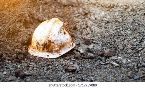An old soiled white plastic safety helmet for an engineer or worker located on gravel ground in a construction area. safety helmet and accident protection . broken helmet