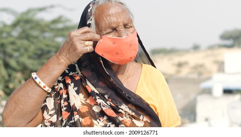 An Old South Asian Woman In Traditional Clothing Putting On A Vibrant Orange Covid-19 Face Mask