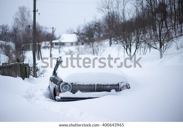 The old\
Soviet car under the snowdrift at the rural scene.\
Photo of a car\
almost totally buried in snow in the\
winter.