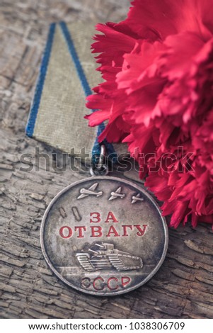 The Old Soviet Medal For Bravery of the Second World War with a red carnation, Victory Day May 9 postcard concept, toned vintage