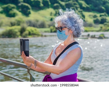 An Old Spanish Woman In A Protective Mask Taking A Selfie Near A Mountain Lake