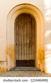 An Old Spanish Wooden Door In A Golden Stucco Archway.