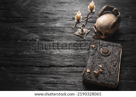 Old spell magic book and burning candle on the wooden table flat lay background with copy space.