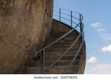 An old spiral staircase made of concrete with cast iron railing, seemingly leading to nowhere or to the sky. Blue sky with clouds, sunny. Stairway to heaven.