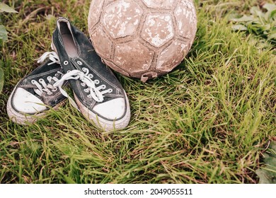 Old Sports Sneakers And A Torn Leather Ball - Worn Out Items And Equipment For Playing Football