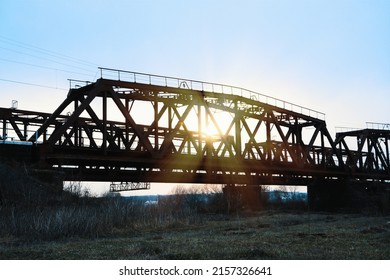 Old steel railway bridge on the river. Empty train-bridge in sunset	
