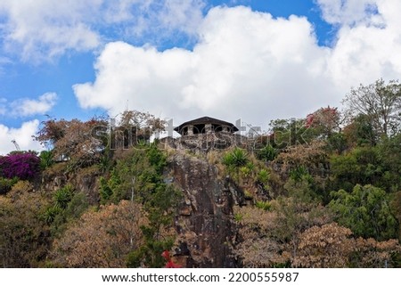 Old stone building on a cliff covered in vegetation and against a cloudy blue sky.