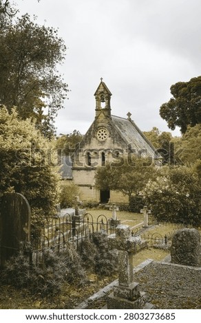 An old stone chapel surrounded by a historic graveyard, set in a lush, green landscape under a cloudy sky.