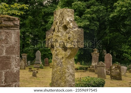 A OLD STONE CROSS IN A CEMETARY IN NIGG SCOTLAND WITH A GREEN TREE LINED BACKGROUND