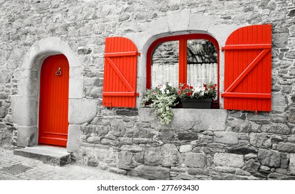 Old stone house with red wooden shutters and red door. Boxes with red and white flowers on the window. Brittany, France. Retro aged photo.  - Powered by Shutterstock