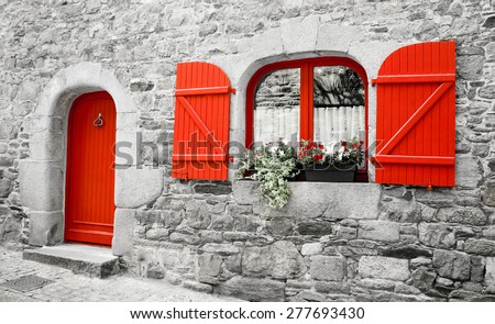 Old stone house with red wooden shutters and red door. Boxes with red and white flowers on the window. Brittany, France. Retro aged photo. 