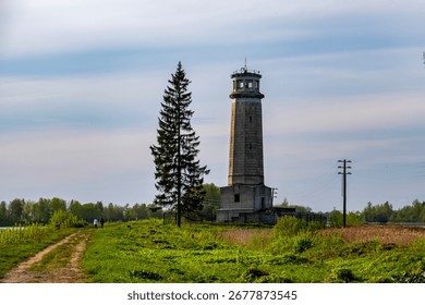 Old stone lighthouse and pine tree on riverside path in spring in Dubna, Russia