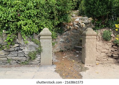 Old stone pillars leading to steps and an overgrown entrance to a suburban house and garden.