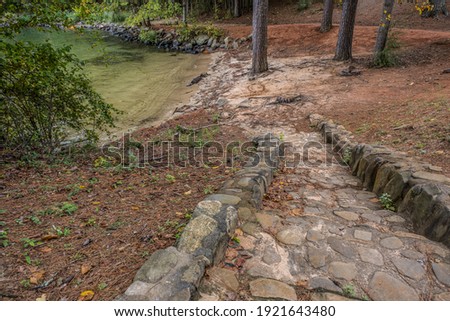 Old stone and rock stairway set in cement descending downhill to the beach area at the lake surrounded by the woodlands on a sunny day in early fall