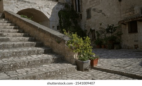 Old stone staircase leads to an archway in matera, basilicata, italy, with vibrant potted plants and historic rustic buildings. - Powered by Shutterstock