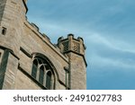 An old stone tower with an arched window against a light blue sky in Cambridge, UK.