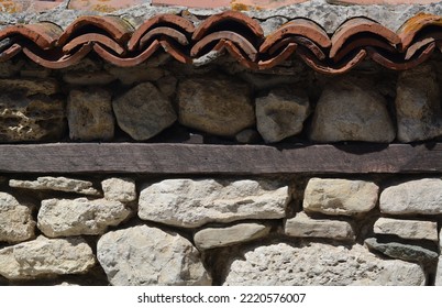 Old stone wall with ceramic tiles roof on sunny day - Shutterstock ID 2220576007
