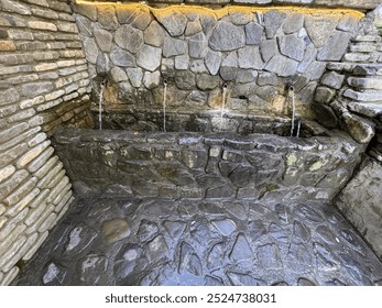 Old stone water fountain. An old stone fountain with many spouts in the park. The four spouts fountain has water flowing into a channel and there are lights on the fountains. Close-up detail. - Powered by Shutterstock