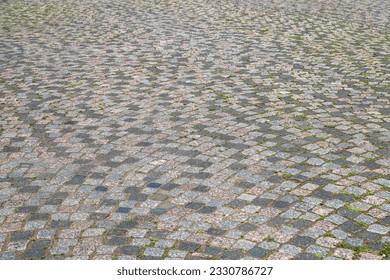 An old stoneblock pavement cobbled in an arc pattern with rectangular granite blocks with green grass between stones. Photo in perspective view with selective focus