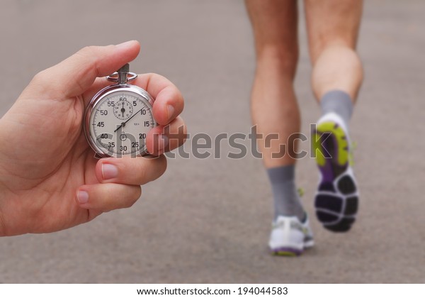 Old stopwatch in a hand and blurred runner athlete\
feet running on a road