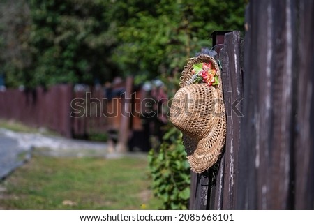 Old straw hat with an artificial flower hangs on a wooden fence on the street at the ethnographic village of Holloko in Hungary, Europe, close up