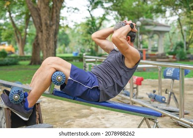 An Old Strong Man Doing Exercise Abdominal Sit-ups At Outdoor Fitness Equipment In The Park, Concept Health Care In Elderly People, Lifestyle  