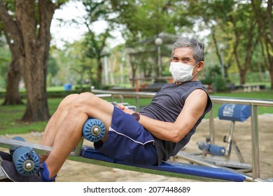 An Old Strong Man With Facemask Doing Exercise By Abdominal Sit-ups At Outdoor Fitness Equipment In The Park, Concept Health Care In Elderly People, Lifestyle 