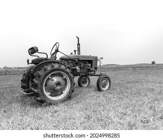 Old Style Farm Trackor Sitting On A Grass Field With A Clear Sky And Rolled Hail Bail In The Distance Edited To Be In Black And White.