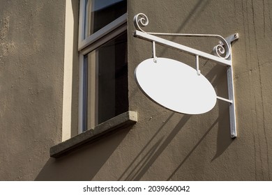 Old Style Oval Metal Sign Board Hanging On A Wall In A Street. White Color And Empty Space For Message. Retro Style Advertisement Theme