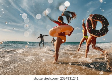 Old style photo of group of friends are having fun and running to sea beach with inflatable donuts