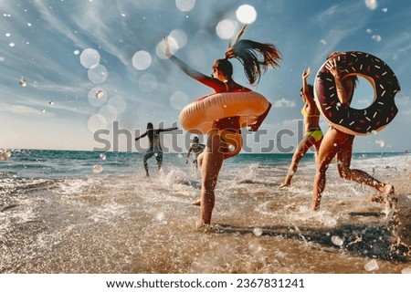 Old style photo of group of friends are having fun and running to sea beach with inflatable donuts