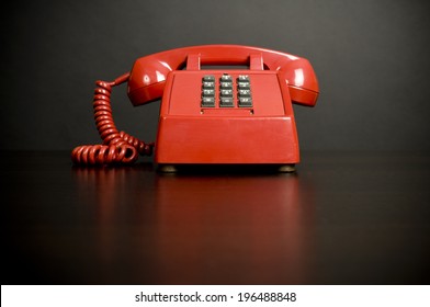 An Old Style Red, Push Button Phone On A Table.