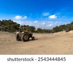 Old style rusty Vintage farm trackor sitting on a field in Jerusalem with a clear sky and green trees. 