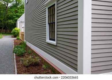 Old Tan Colored House With White Trim And Black Wood Window Frame Spacers. The Glass In The Window Is Wavy And Reflects The Sun. The Exterior Wall Is Made Of Vintage Beige Cape Cod Clapboard Siding.