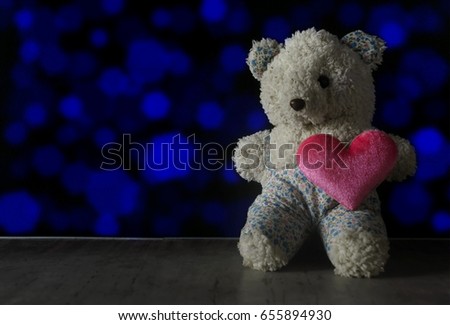 Old teddy bear one eye and blurred pink heart on old table with bokeh background, dark tone style, copy space.