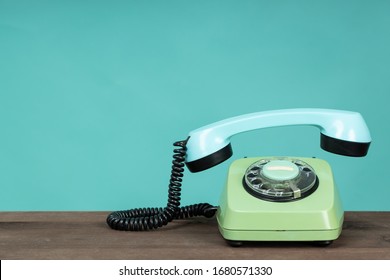 Old telephone on wooden table in front of green background. Vintage phone with taken off receiver. Vintage style photo.
