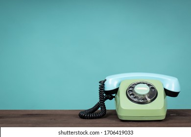 Old telephone on wooden table in front of green background. Vintage phone