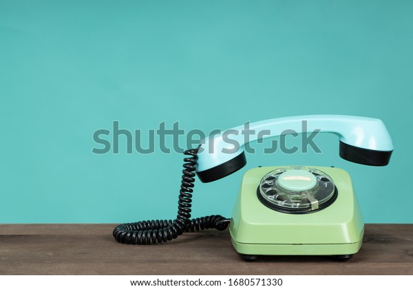 Old\
telephone on wooden table in front of green background. Vintage\
phone with taken off receiver. Vintage style photo.\
