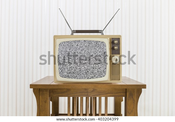 Old television with antenna on wood table with\
static screen.