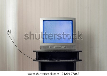 Old television blue empty screen with broken signal was recently placed on the table along with cord in the style of 1970s, light gray and dark blue matte photo. Retro tv on wooden nightstand in room