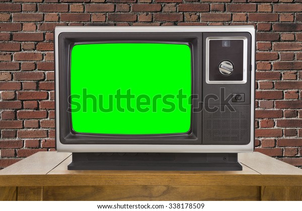 Old television with chroma key green screen and\
brick wall.