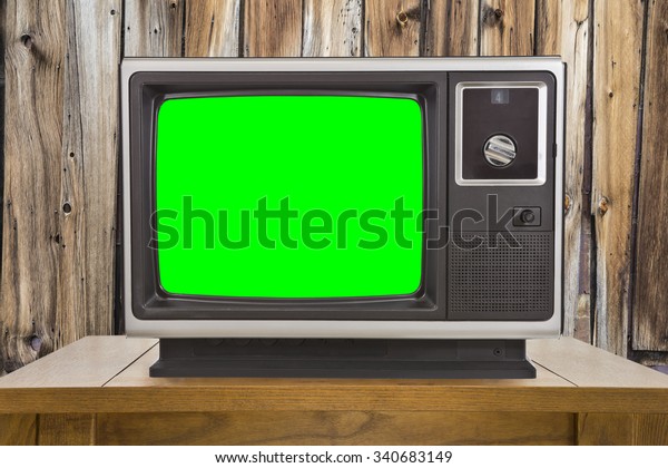 Old television with chroma key green screen and\
rustic wood wall.
