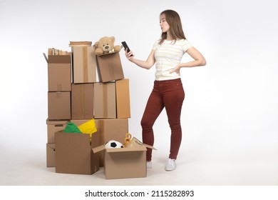 Old things in boxes. Girl with boxes on light. Woman thinking about storage space concept. Girl looking for place for personal storage. Unnecessary personal items in front of woman. Girl with phone