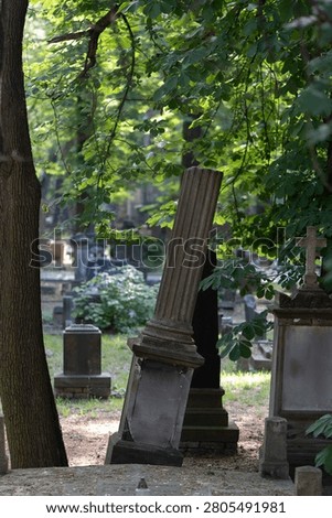 Old tilted column monument stands on a grave inside a cemetery yard. Historical churchyard tombstone represents decay, passing of time, funeral mourning and graveyard heritage conservation.