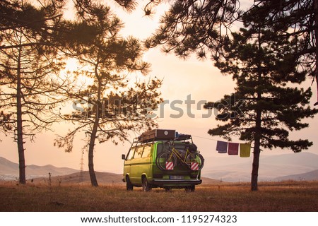 Old timer camper van parked on the top of the hill between pine trees in the beautiful sunset sky