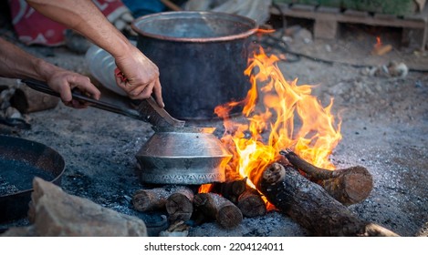 Old Tinned Copper Pot Being Cleaned With A Wire Brush Over A Log Burning Fire On The Floor