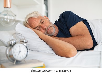 Old tired man sleeping on bed at home. Senior man with white hair in deep sleep on soft pillow at home. Mature healthy guy lying on side resting at home while sleeping.